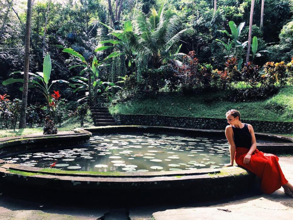 Woman sits on the edge of a fountain surrounded by forest in the Goa Gajah temple in Bali