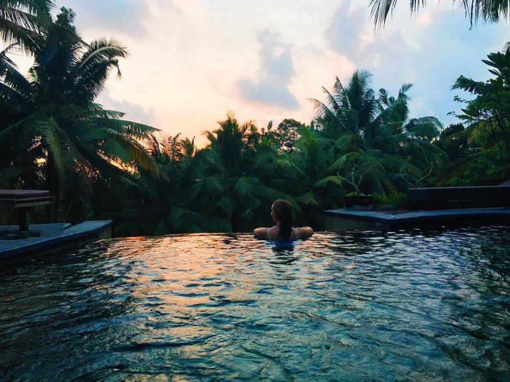 Woman facing the forest at the edge of an infinity pool in Ubud, Bali at sunset