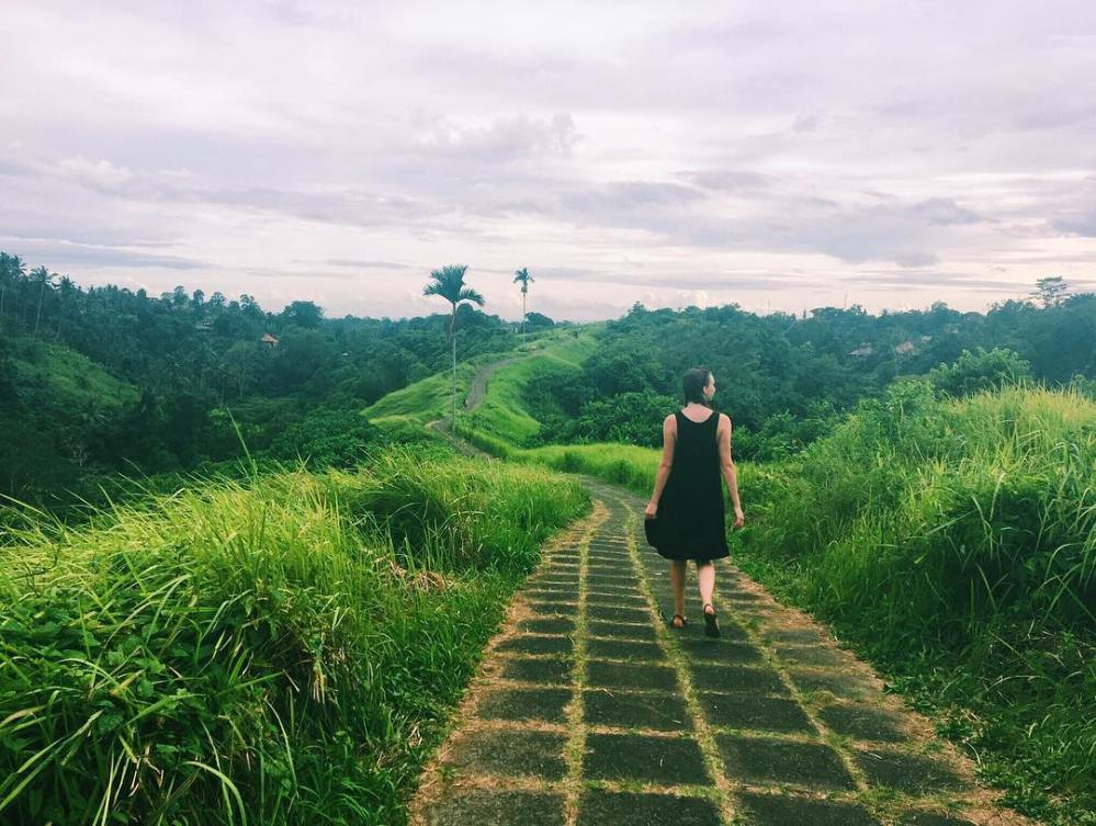 Woman strolls along cobblestone path through the fields of Ubud, Bali